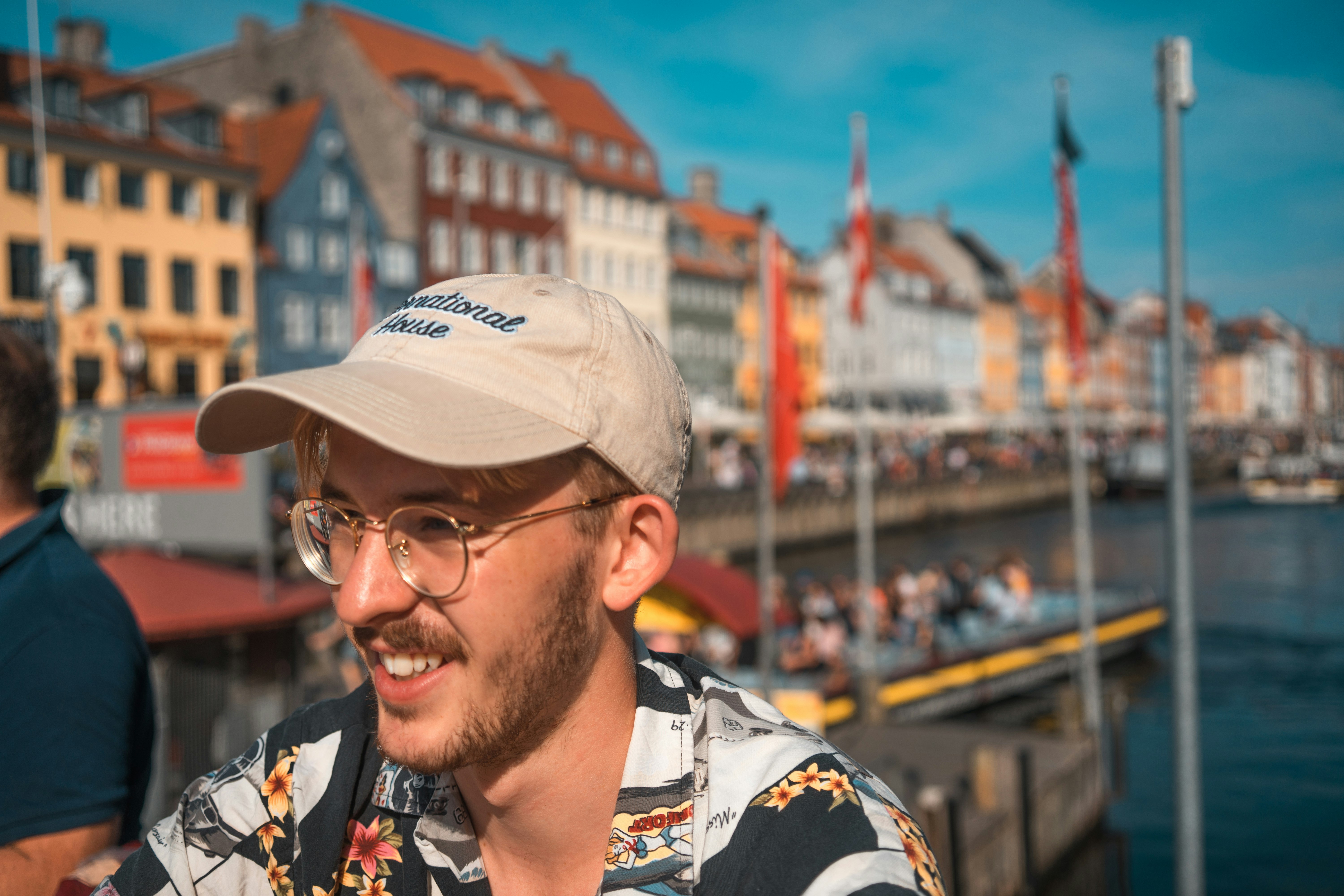 man wearing multicolored collared shirt and eyeglasses smiling near body of water during daytime